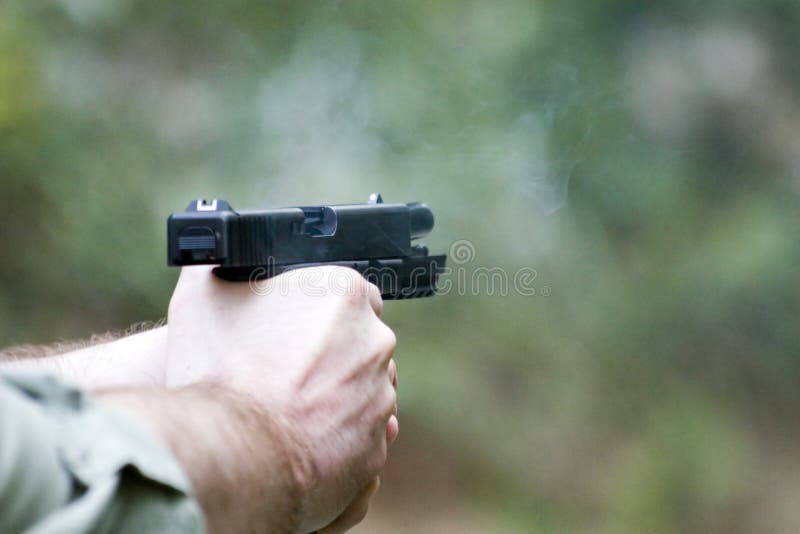 Hands of person shooting gun or pistol with slide back and empty magazine; green nature background. Hands of person shooting gun or pistol with slide back and empty magazine; green nature background.