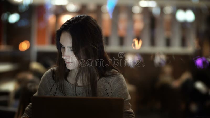 年轻人在晚上集中了工作在咖啡馆的妇女 使用膝上型计算机的深色的女性和谈话在电话