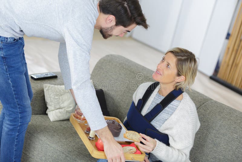 男士为受伤的女士端来托盘里的食物 免版税库存照片