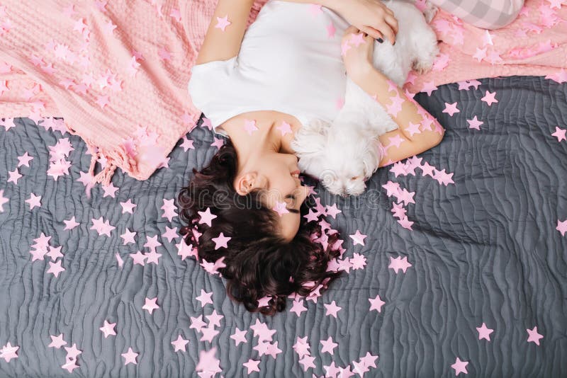 从俏丽的妇女上的看法变冷与在床上的小犬座的睡衣的与桃红色毯子 享用在家在桃红色放松 库存图片 从俏丽的妇女上的看法变冷与在床上的小犬座的睡衣的与桃红色毯子 享用在家在桃红色放松 库存图片