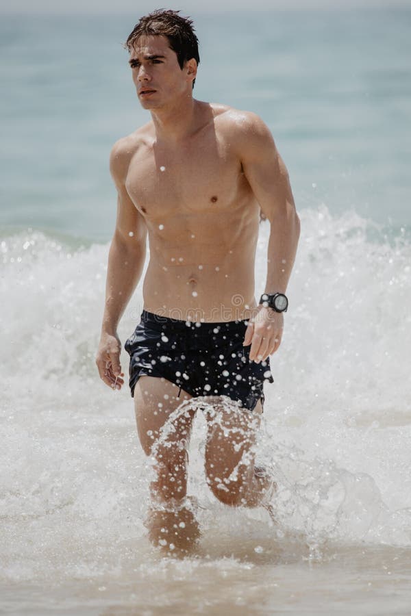 从在一个热带海滩的年轻英俊的肌肉人水走出去穿着游泳衣