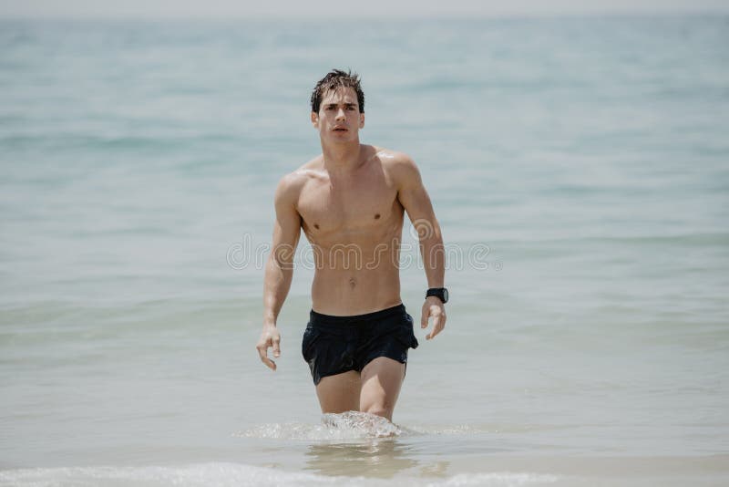 从在一个热带海滩的年轻英俊的肌肉人水走出去穿着游泳衣