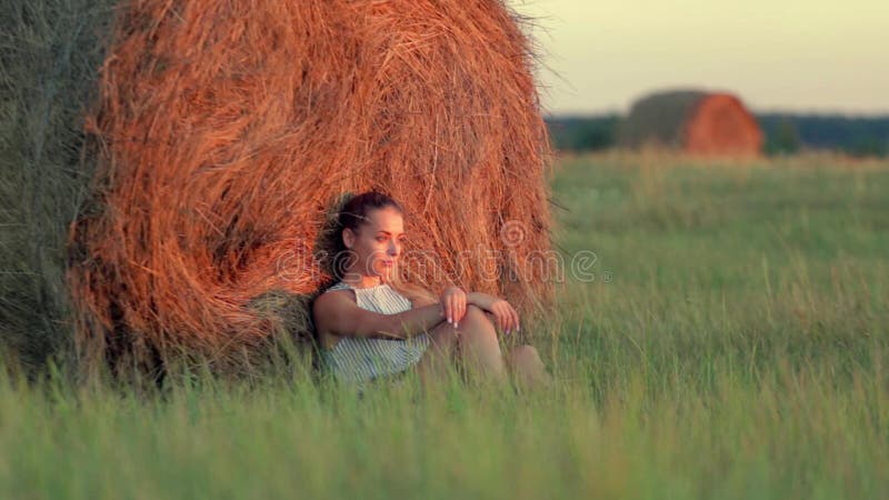 休息在堆的美丽的女孩干草在日落