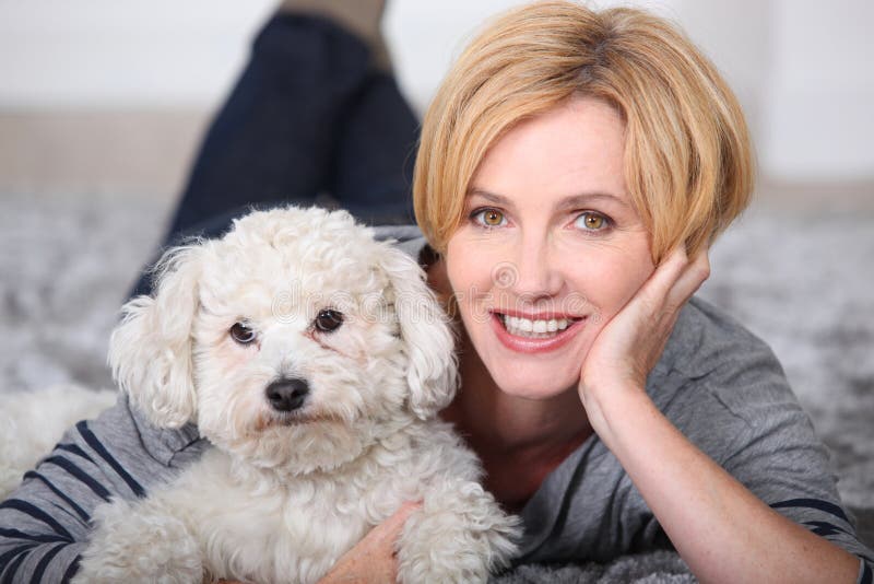 Blonde woman lying on the carpet with a small fluffy white dog. Blonde woman lying on the carpet with a small fluffy white dog