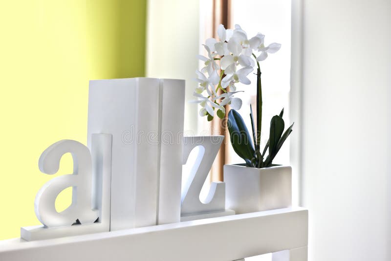 House interior decoration using 3d English letters and a white flowering plant, all letters and the supporter of the decor is white and made of wooden or cement, the background is blurred a little and probably near to the window. House interior decoration using 3d English letters and a white flowering plant, all letters and the supporter of the decor is white and made of wooden or cement, the background is blurred a little and probably near to the window