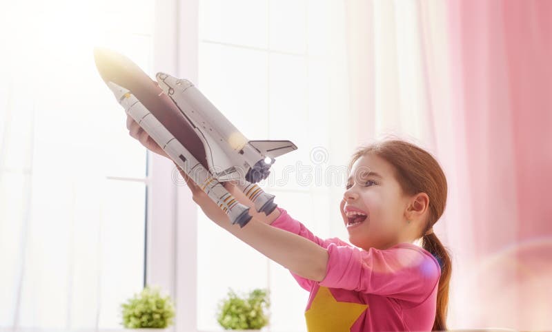 Child girl playing with toy rocket and dreaming of becoming a spacemen. Portrait of funny kid near windows. Child girl playing with toy rocket and dreaming of becoming a spacemen. Portrait of funny kid near windows.