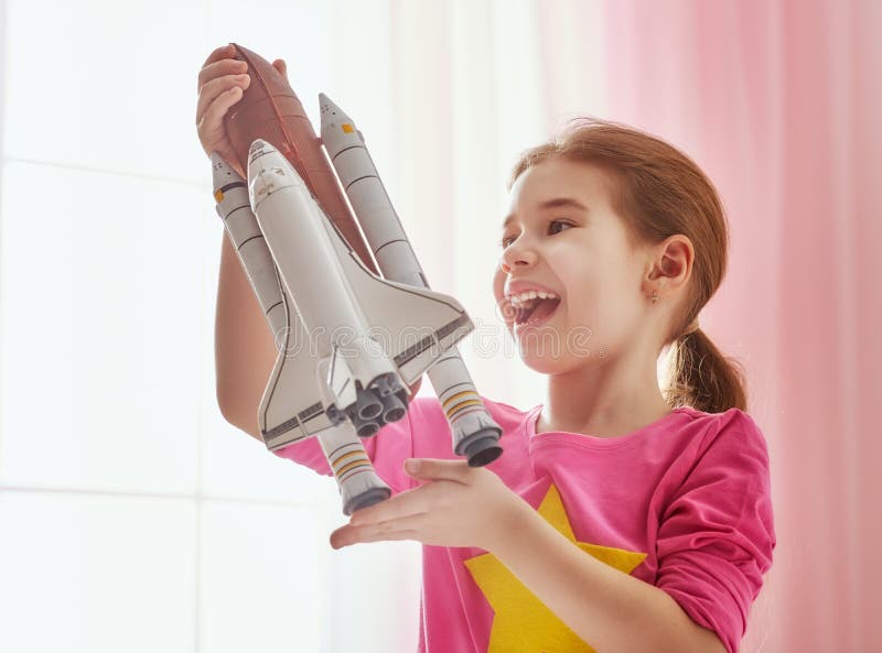 Child girl playing with toy rocket and dreaming of becoming a spacemen. Portrait of funny kid near windows. Child girl playing with toy rocket and dreaming of becoming a spacemen. Portrait of funny kid near windows.