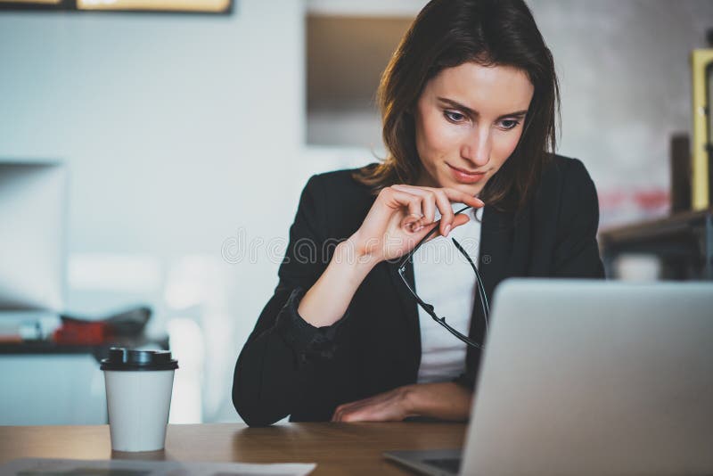 使用便携式计算机的微笑的美丽的女实业家在现代办公室 被弄脏的背景 水平 库存照片