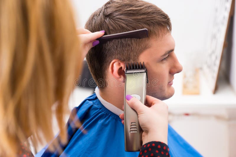 Close Up Profile of Blond Female Stylist with Painted Finger Nails Using Electric Razor to Cut and Style Hair of Young Male Client in Salon. Close Up Profile of Blond Female Stylist with Painted Finger Nails Using Electric Razor to Cut and Style Hair of Young Male Client in Salon