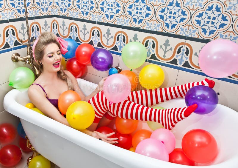 Blonde woman playing in her bath tube with bright colored balloons. Sensual girl with white and red striped stockings having fun in bathroom, covered with balloons. Blonde woman playing in her bath tube with bright colored balloons. Sensual girl with white and red striped stockings having fun in bathroom, covered with balloons