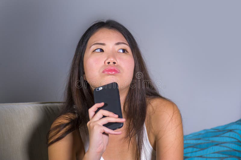 使用在手机的年轻甜愉快和相当亚裔韩国女孩互联网社会媒介app看起来周道和沉思sitt 免版税库存照片