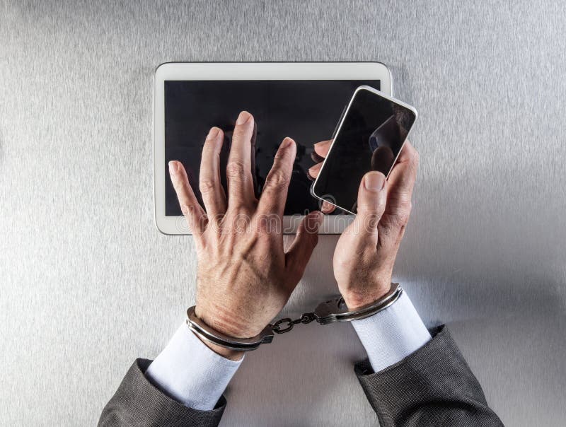 Anonymous workaholic businessman tied to communications handcuffs using a digital tablet and mobile phone for concept of modern slavery, hostage or victim of company technology obsession, above view. Anonymous workaholic businessman tied to communications handcuffs using a digital tablet and mobile phone for concept of modern slavery, hostage or victim of company technology obsession, above view