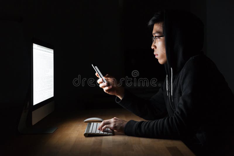 使用膝上型计算机和手机的黑客在暗室 免版税库存图片 使用膝上型计算机和手机的黑客在暗室 免版税库存图片