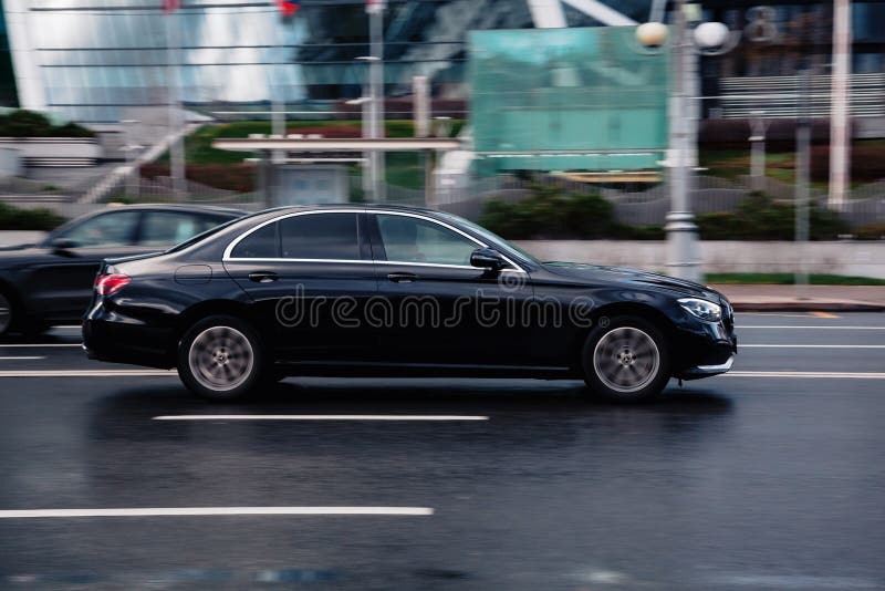 Moscow, Russia - October 2021: Side view Mercedes Benz E Class W213 Facelift car moving on wet slippery city road. Driver in black sedan E-Class rushes for job. Moscow, Russia - October 2021: Side view Mercedes Benz E Class W213 Facelift car moving on wet slippery city road. Driver in black sedan E-Class rushes for job