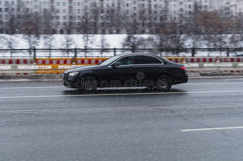 Moscow, Russia - december 2021: Side view Mercedes Benz E Class W213 Facelift car moving on wet slippery city road. Black Mercedes E 450 4MATIC is driving on the winter street during snowfall. Moscow, Russia - december 2021: Side view Mercedes Benz E Class W213 Facelift car moving on wet slippery city road. Black Mercedes E 450 4MATIC is driving on the winter street during snowfall