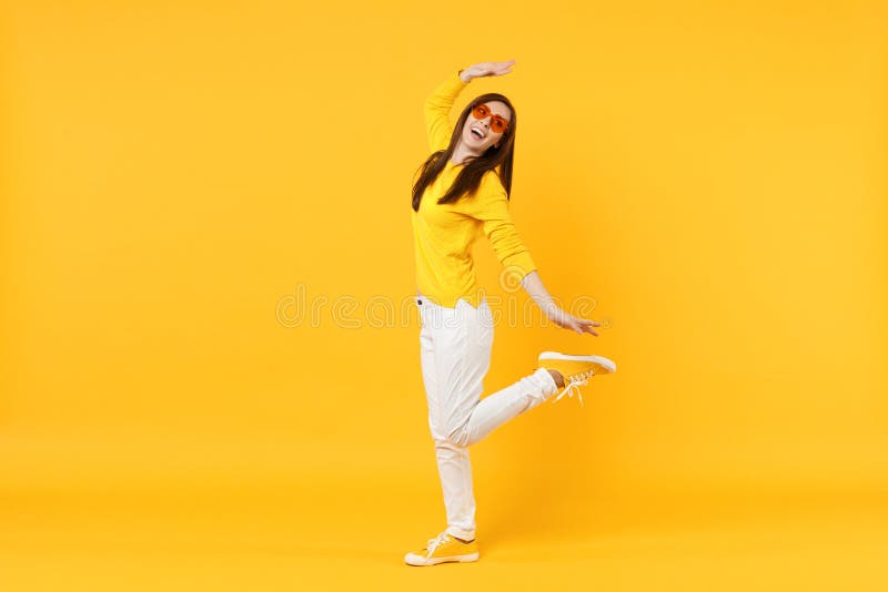 便服的,看在旁边传播的手的心脏玻璃快乐的年轻女人隔绝在橙黄墙壁上 图库摄影 便服的,看在旁边传播的手的心脏玻璃快乐的年轻女人隔绝在橙黄墙壁上 图库摄影