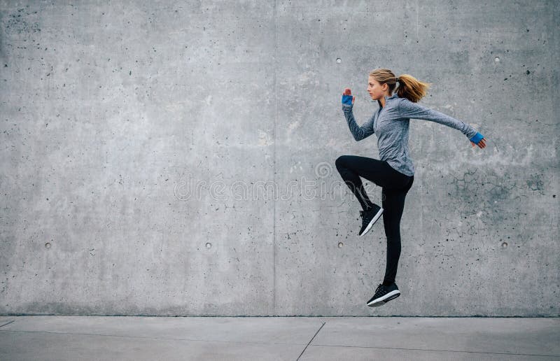 Side view shot of fit young woman doing cardio interval training against grey background. Fitness female exercising outdoors in morning. Side view shot of fit young woman doing cardio interval training against grey background. Fitness female exercising outdoors in morning.