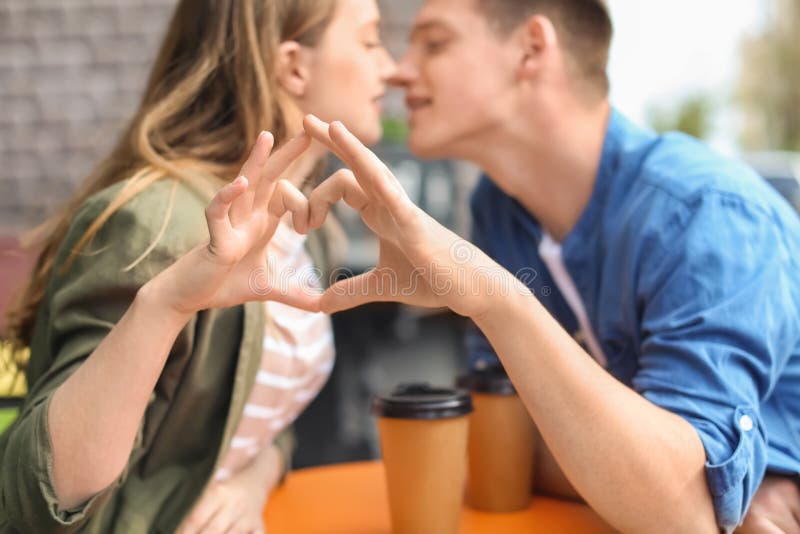 做心脏用他们的手的愉快的年轻夫妇,当坐在街道咖啡馆时 库存图片 做心脏用他们的手的愉快的年轻夫妇,当坐在街道咖啡馆时 库存图片