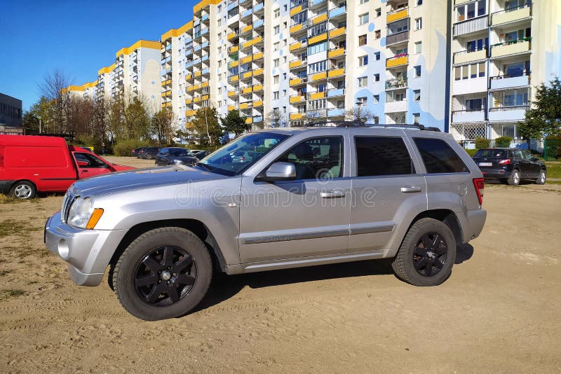 Silver modern Jeep Cherokee four wheel drive private car parked on sandy parking with post communist blocks of flats in Gdansk, Poland, in the background. Front and left side view, four doors vehicle popular nowadays. Evening low sunlight in spring time. Post communist blocks of flats in Gdansk in the background. Silver modern Jeep Cherokee four wheel drive private car parked on sandy parking with post communist blocks of flats in Gdansk, Poland, in the background. Front and left side view, four doors vehicle popular nowadays. Evening low sunlight in spring time. Post communist blocks of flats in Gdansk in the background.