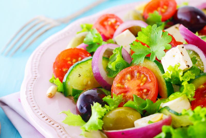 Healthy fresh salad with feta cheese , crispy lettuce, cherry tomato, onion rings, cucumber and olives on a white plate. Healthy fresh salad with feta cheese , crispy lettuce, cherry tomato, onion rings, cucumber and olives on a white plate