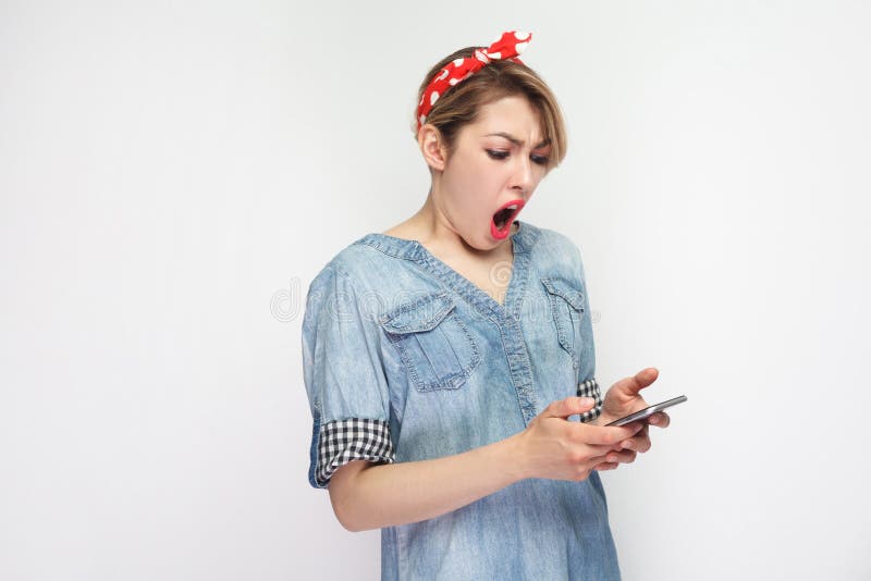 偶然蓝色牛仔布衬衣的震惊美丽的博客作者年轻女人有构成、红色头饰带身分,用途智能手机和观看的 免版税库存图片 偶然蓝色牛仔布衬衣的震惊美丽的博客作者年轻女人有构成、红色头饰带身分,用途智能手机和观看的 免版税库存图片