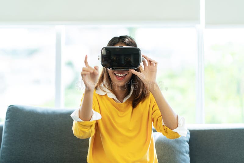 偶然黄色衬衣的年轻亚裔妇女戴VR眼镜观看录影的或喜欢演奏感觉的计算机游戏激发 免版税图库摄影 偶然黄色衬衣的年轻亚裔妇女戴VR眼镜观看录影的或喜欢演奏感觉的计算机游戏激发 免版税图库摄影