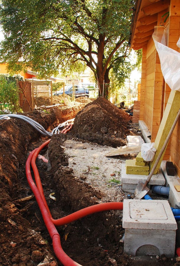 A utilities trench at the side of a newly build wood (fir) house. The trench carries the conduits for gas, water, electric, sewage and phone services. The water and sewage inspection chambers can be seen in the foreground right. A utilities trench at the side of a newly build wood (fir) house. The trench carries the conduits for gas, water, electric, sewage and phone services. The water and sewage inspection chambers can be seen in the foreground right