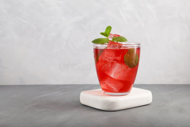 Iced fruit tea or cold watermelon drink in clear glass with mint leaf. Refreshing summer drink. Grey background, copy space. Iced fruit tea or cold watermelon drink in clear glass with mint leaf. Refreshing summer drink. Grey background, copy space.