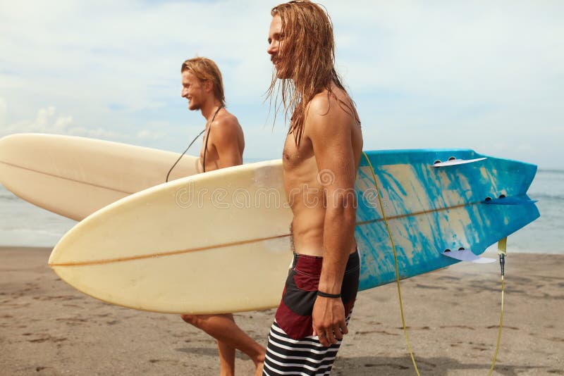 Surfing. Handsome Surfers With Surfboards. Young Men Walking On Ocean Beach. Active Lifestyle, Water Sport On Beautiful Sea Background. Surfing. Handsome Surfers With Surfboards. Young Men Walking On Ocean Beach. Active Lifestyle, Water Sport On Beautiful Sea Background