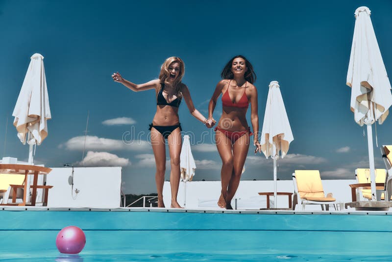 Full length of two attractive young women in bikini preparing to jump into the pool. Full length of two attractive young women in bikini preparing to jump into the pool