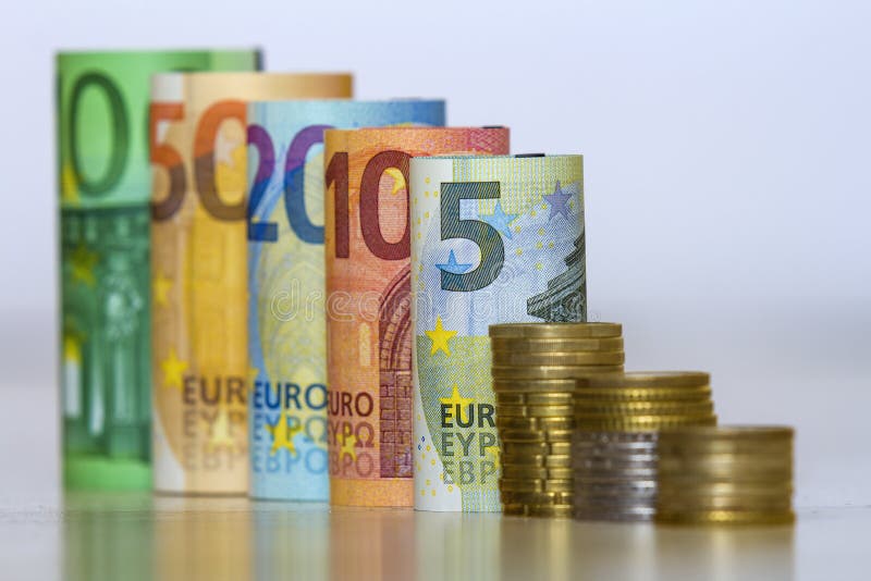 Straight row of accurately rolled hundred, fifty, twenty, ten and five new paper euro banknotes and pile of metallic coins isolated on white background. Symbol of financial prosperity, wealth and success. Straight row of accurately rolled hundred, fifty, twenty, ten and five new paper euro banknotes and pile of metallic coins isolated on white background. Symbol of financial prosperity, wealth and success.