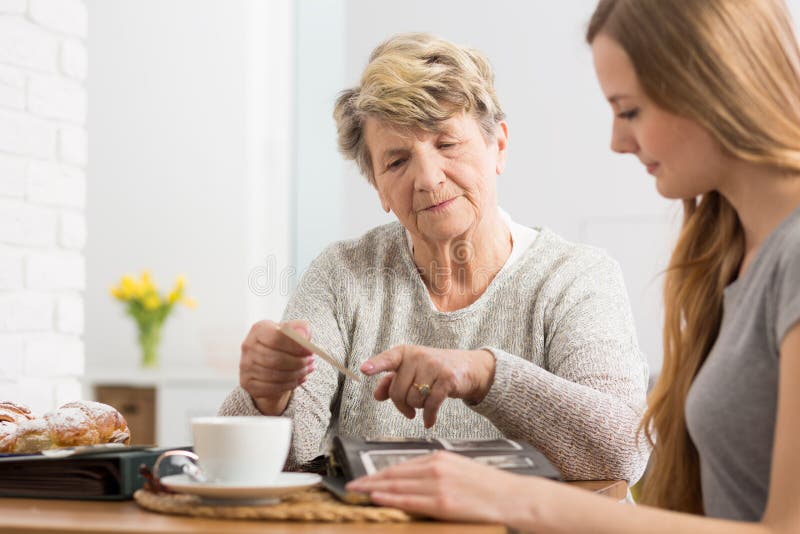 Portrait of an elderly lady having coffee with her granddaughter and showing an old photograph to her. Portrait of an elderly lady having coffee with her granddaughter and showing an old photograph to her