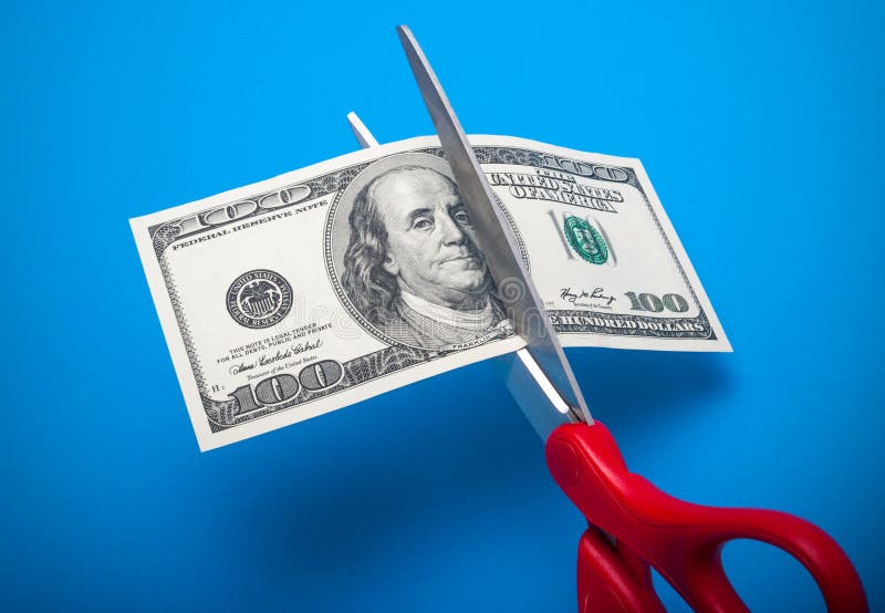 100 dollar bill being cut with scissors isolated on a blue background. 100 dollar bill being cut with scissors isolated on a blue background