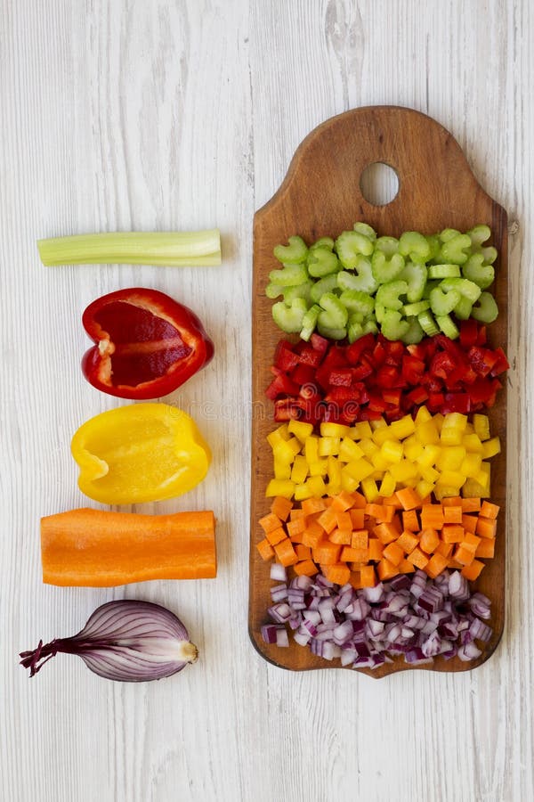 Chopped fresh vegetables carrot, celery, onion, colored peppers arranged on cutting board on a white wooden surface, top view. Overhead, from above. Chopped fresh vegetables carrot, celery, onion, colored peppers arranged on cutting board on a white wooden surface, top view. Overhead, from above.