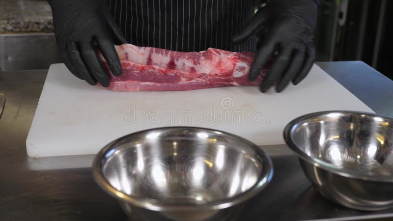 切板上一位戴手套切鲜猪肉的厨师的特写. 股票视频