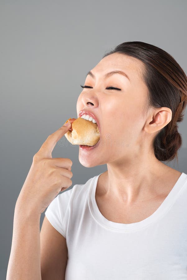 Vertical image of a greedy young woman eating a hot dog to the very last bit of it. Vertical image of a greedy young woman eating a hot dog to the very last bit of it
