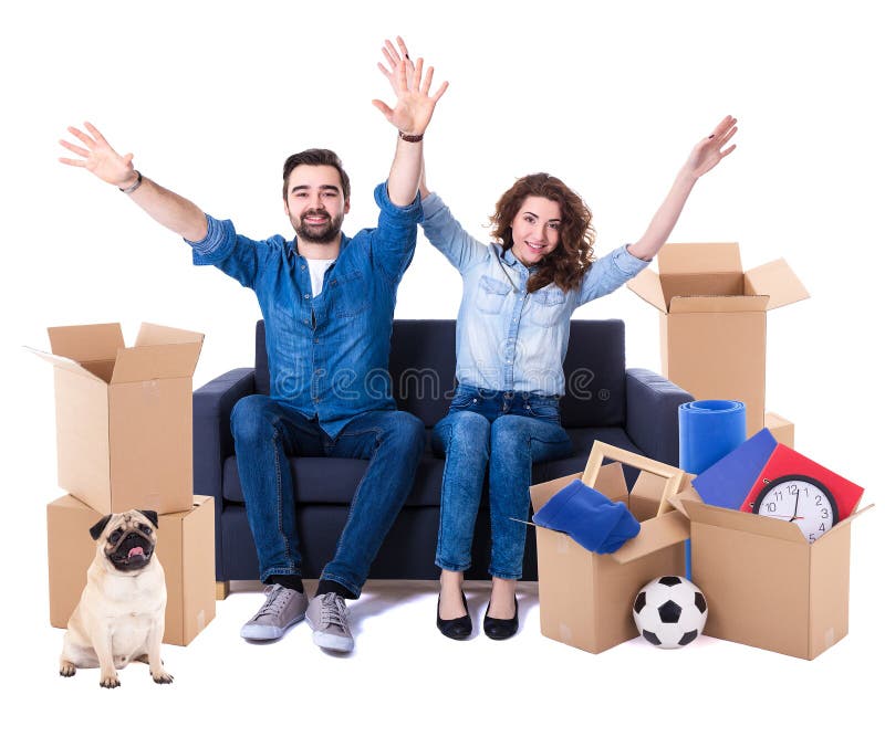 Moving day and new home concept - cheerful couple sitting on sofa with brown cardboard boxes and dog isolated on white background. Moving day and new home concept - cheerful couple sitting on sofa with brown cardboard boxes and dog isolated on white background