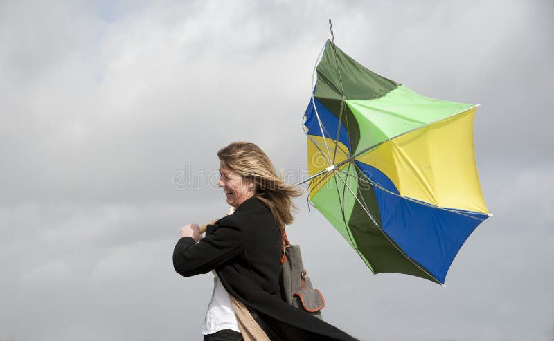 Woman struggles to hold onto her inside out umbrella on a windy day. Woman struggles to hold onto her inside out umbrella on a windy day