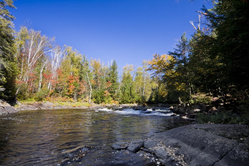 A set of rapids in a small river . Taken on a bright sunny fall day, with blue skies and beginnings of fall colour. A set of rapids in a small river . Taken on a bright sunny fall day, with blue skies and beginnings of fall colour.