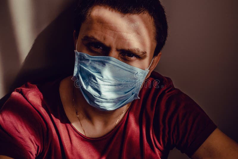 医用面具中伤心的成年男子画像坐在墙上凝视着 在家保持隔离 隔离 库存照片