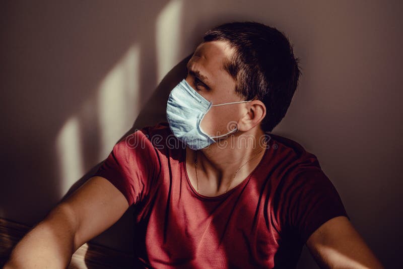 医用面具斜墙上光影图案的伤心成年男子侧像 在家保持隔离 库存图片