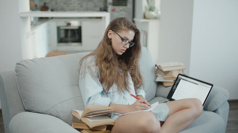 十几岁的女孩在膝上型计算机在笔记本读，写，为检查或家庭作业做准备，全部书