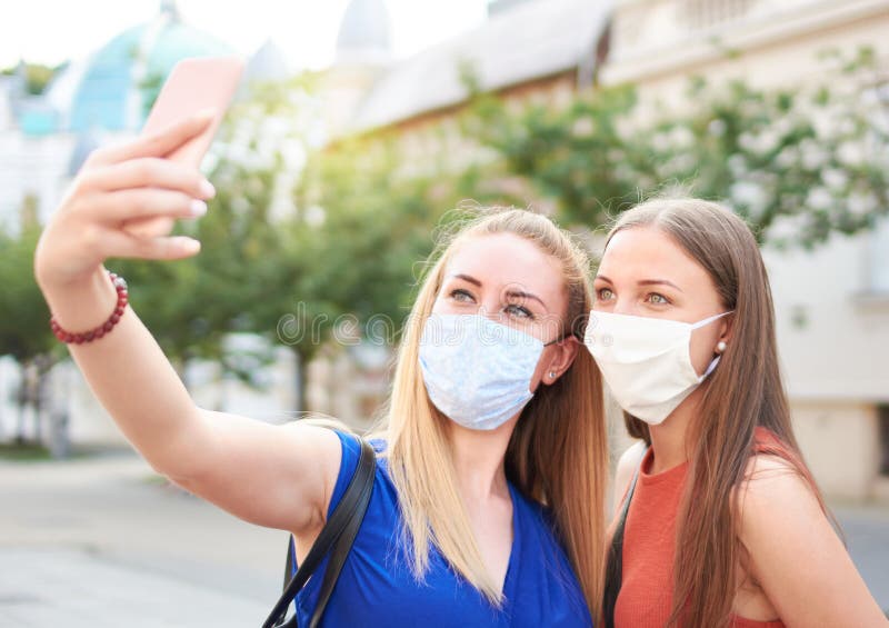 千禧一代的女性朋友戴着口罩笑着自拍 - 新常态夏季友谊概念，年轻女孩们玩得很开心 库存照片