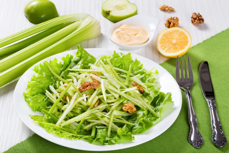 Studio macro of Salad with Green apples, Celery and walnut on a bed of lettuce on a white dish, on white wooden background, american cuisine, view from above. Studio macro of Salad with Green apples, Celery and walnut on a bed of lettuce on a white dish, on white wooden background, american cuisine, view from above