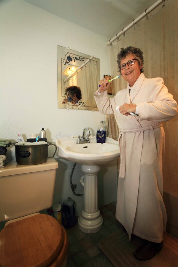 An older woman in a long housecoat standing in the bathroom getting ready to brush her teeth. An older woman in a long housecoat standing in the bathroom getting ready to brush her teeth.