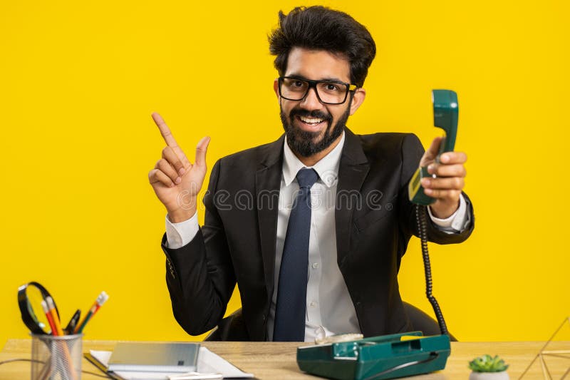 Hey you, call me back. Indian businessman talking on wired retro vintage telephone of 80s at office workplace desk. Hindu in formal suit. Remote distant online working on laptop on yellow background. Hey you, call me back. Indian businessman talking on wired retro vintage telephone of 80s at office workplace desk. Hindu in formal suit. Remote distant online working on laptop on yellow background