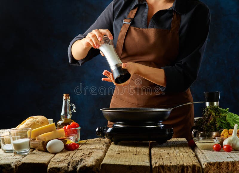 厨师在煎锅里把香料加到鸡肉片上. 制作经典凯撒沙拉的过程. 所有的成分都在 免版税图库摄影
