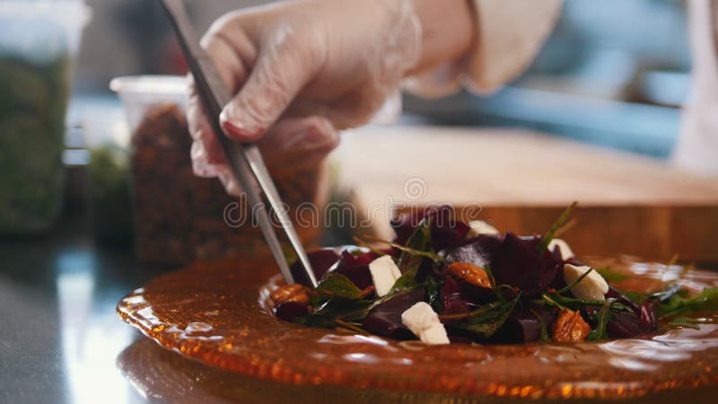 厨师通过安置组分在板材和放置有镊子的坚果供食沙拉