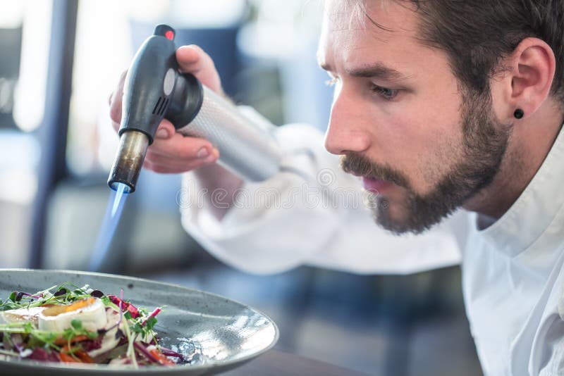 Chef preparing food. Cook flamed using Flambé gun pistol. Chef flambe vegetable salad with goat cheese. Gourmet cuisine. Chef preparing food. Cook flamed using Flambé gun pistol. Chef flambe vegetable salad with goat cheese. Gourmet cuisine.