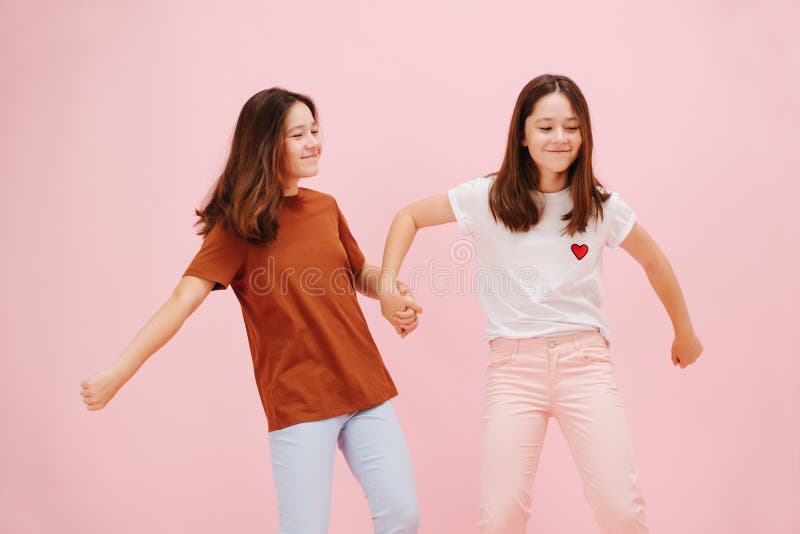 友爱的小双胞胎姐妹高兴地牵着粉红的手 免版税库存图片